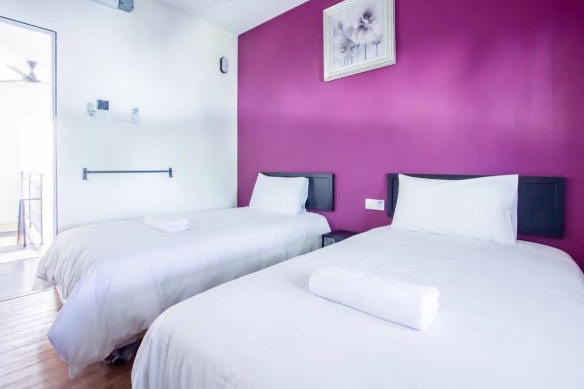 Ett hotellrum med två sängar, en lila accentvägg och ett stort fönster.