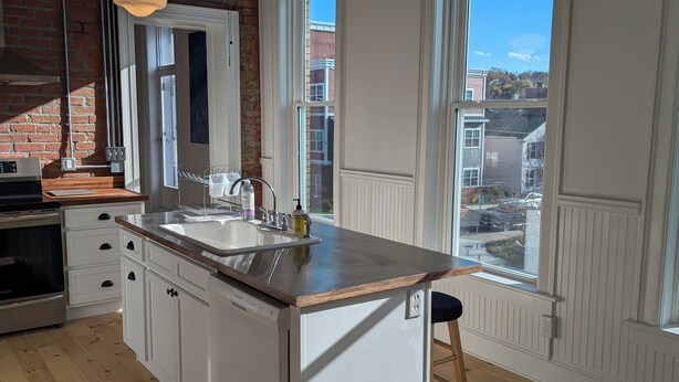 A kitchen with a large island, wooden flooring, and a view of the city through large windows.