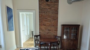 A living room with a brick wall, a round wooden table, a cushioned armchair, a patterned rug, and a wooden cabinet.