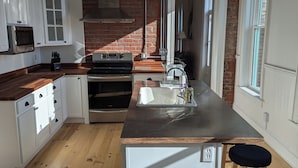 A modern kitchen with a brick wall, white cabinetry, a stainless steel sink, and a wooden island.