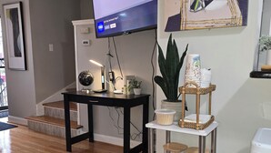 A living room with a flat-screen TV mounted on the wall, a black coffee table with a lamp, a white shelving unit with decorative items, and a wooden floor. - A Pleasant Stay (Oak Park)