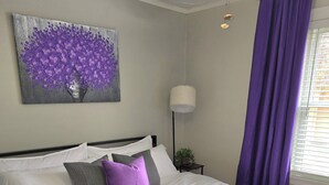 A bedroom with a bed, a ceiling fan, a window with purple curtains, and a wall-mounted painting. - A Pleasant Stay (Oak Park)