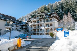 Een meerhoog hotel met balkons, een besneeuwde ingang en een bord dat een skigebied aangeeft.