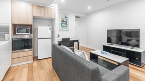 A modern kitchen with a microwave, oven, and refrigerator, a gray sofa, a flat-screen TV, and a dining table. - Serain Residences Canberra Centre (Braddon)