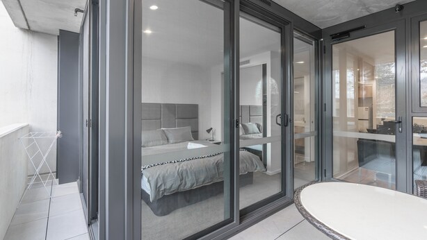 A modern bedroom with a large bed, a bathroom with a bathtub, and a balcony with a drying rack. - Serain Residences Canberra Centre (Braddon)
