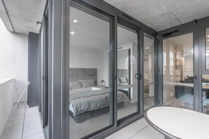 A modern bedroom with a large bed, a bathroom with a bathtub, and a balcony with a drying rack. - Serain Residences Canberra Centre (Braddon)