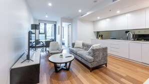 A modern living room with a sofa, chairs, a coffee table, and a kitchen area with white cabinets and a countertop. - Serain Residences Canberra Centre (Braddon)