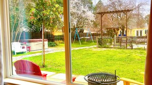A view from a window to a backyard with a swing set, a grill, and a lawn.