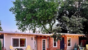 A house with a front porch, two windows, and a door. There are two chairs and a small table on the porch.