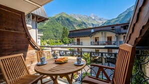 A wooden deck with a round table and chairs, overlooking a mountain landscape. - Le Cristal MB8 Mountain View, Pool, Parking & Free WiFi, Argentière (Chamonix), France (Argentière (Chamonix))