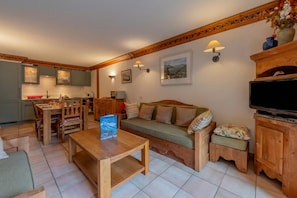 Una sala de estar acogedora con un sofá de madera, una mesa de comedor y una cocina con armarios y un televisor.