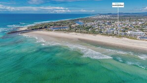 Vista aerea di una zona costiera con acque cristalline turchesi, una spiaggia sabbiosa e una zona residenziale con case e vegetazione.