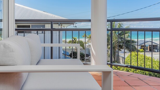 Un balcone con un divano bianco, vista sulla spiaggia e cielo sereno.