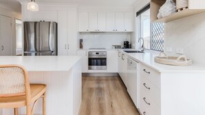 Una cucina moderna con mobili bianchi, elettrodomestici in acciaio inossidabile, un tavolo da pranzo in legno e una sedia in fibra.