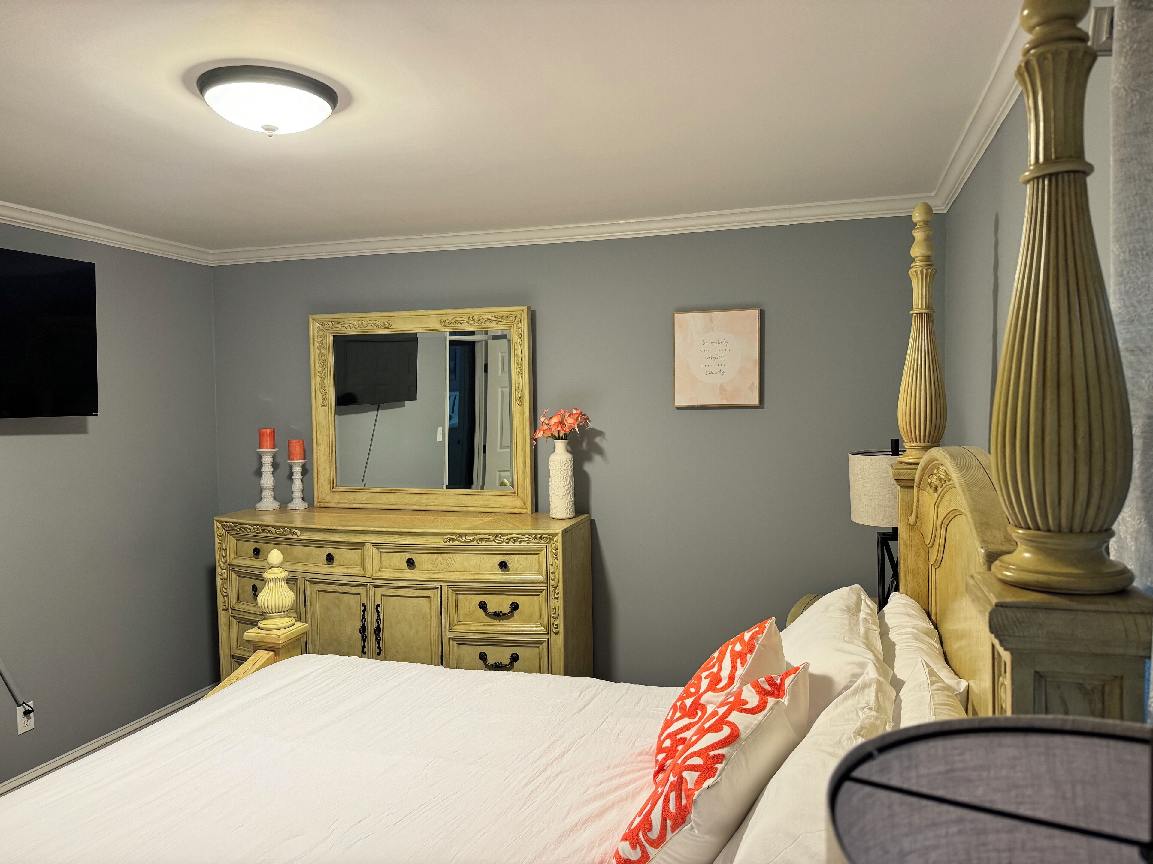 A bedroom with a bed, a dresser, a mirror, and a bedside table.
