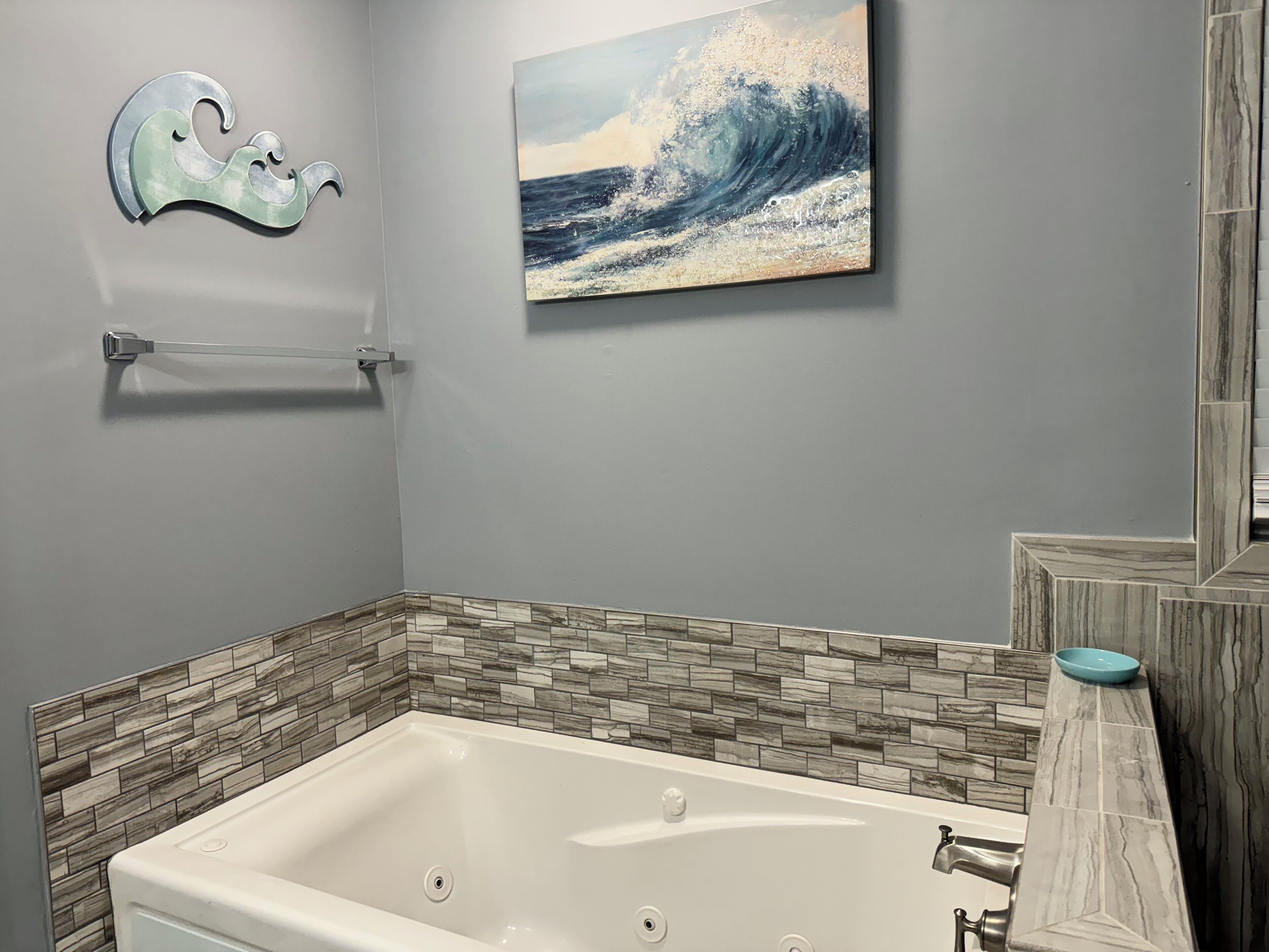 Un baño con bañera, un perchero, un cuadro de una ola y un salpicadero de azulejos.