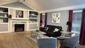 Un salon moderne avec une cheminée, un canapé noir, des fauteuils gris et une table basse.