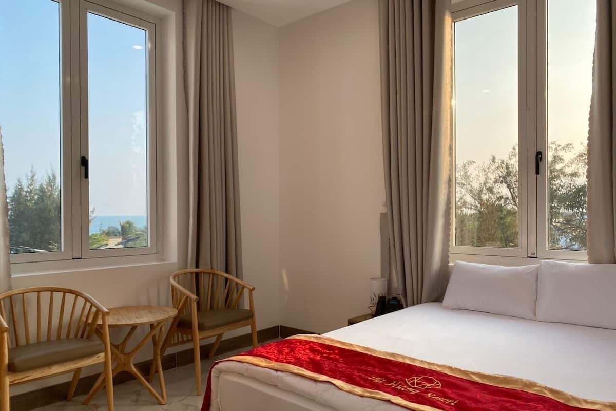 Une chambre d’hôtel comprenant un lit, deux chaises, une table et de grandes fenêtres donnant sur l’extérieur.