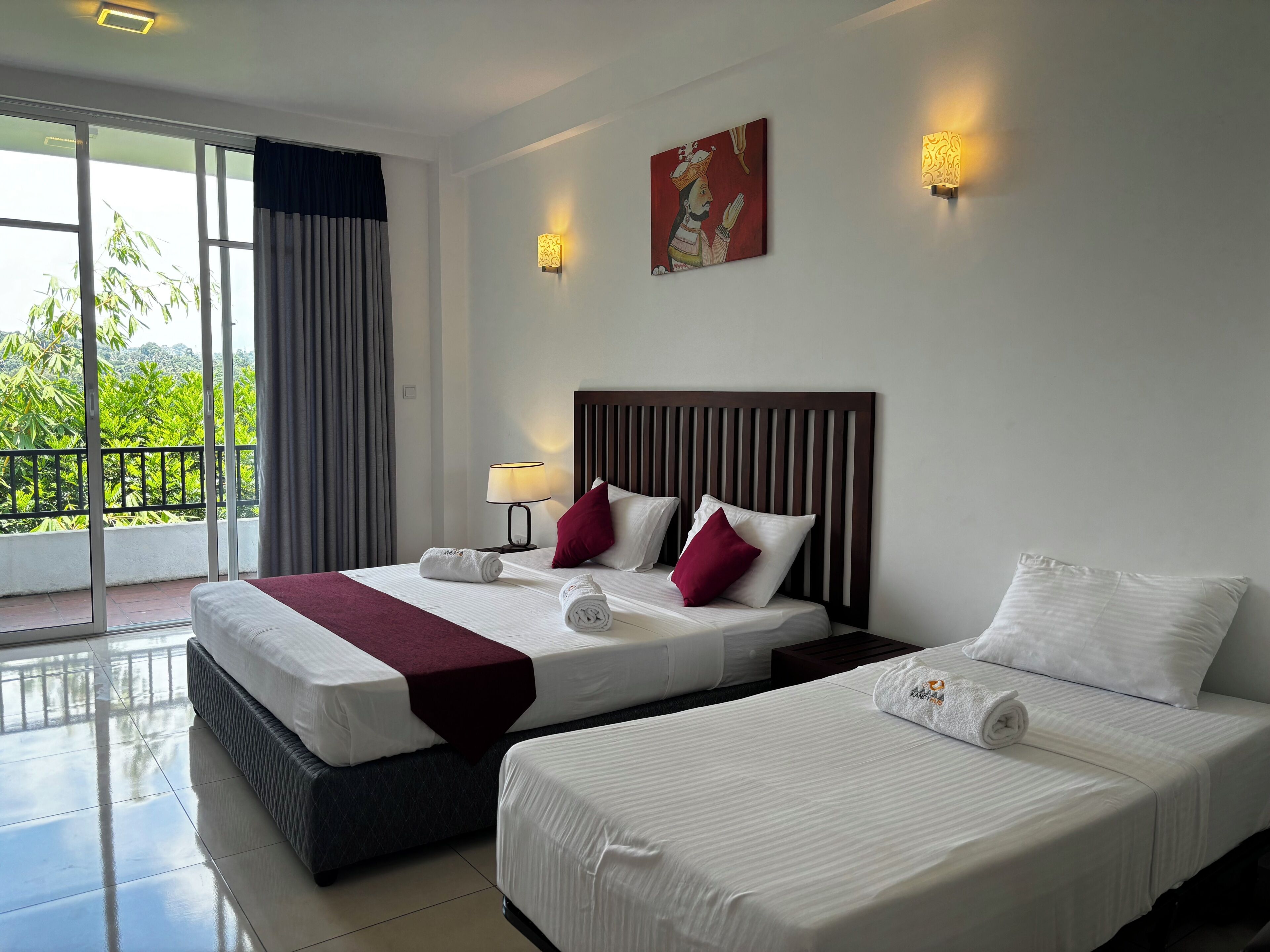 A hotel room with two beds, a balcony with a view, a painting on the wall, and two wall-mounted lights.