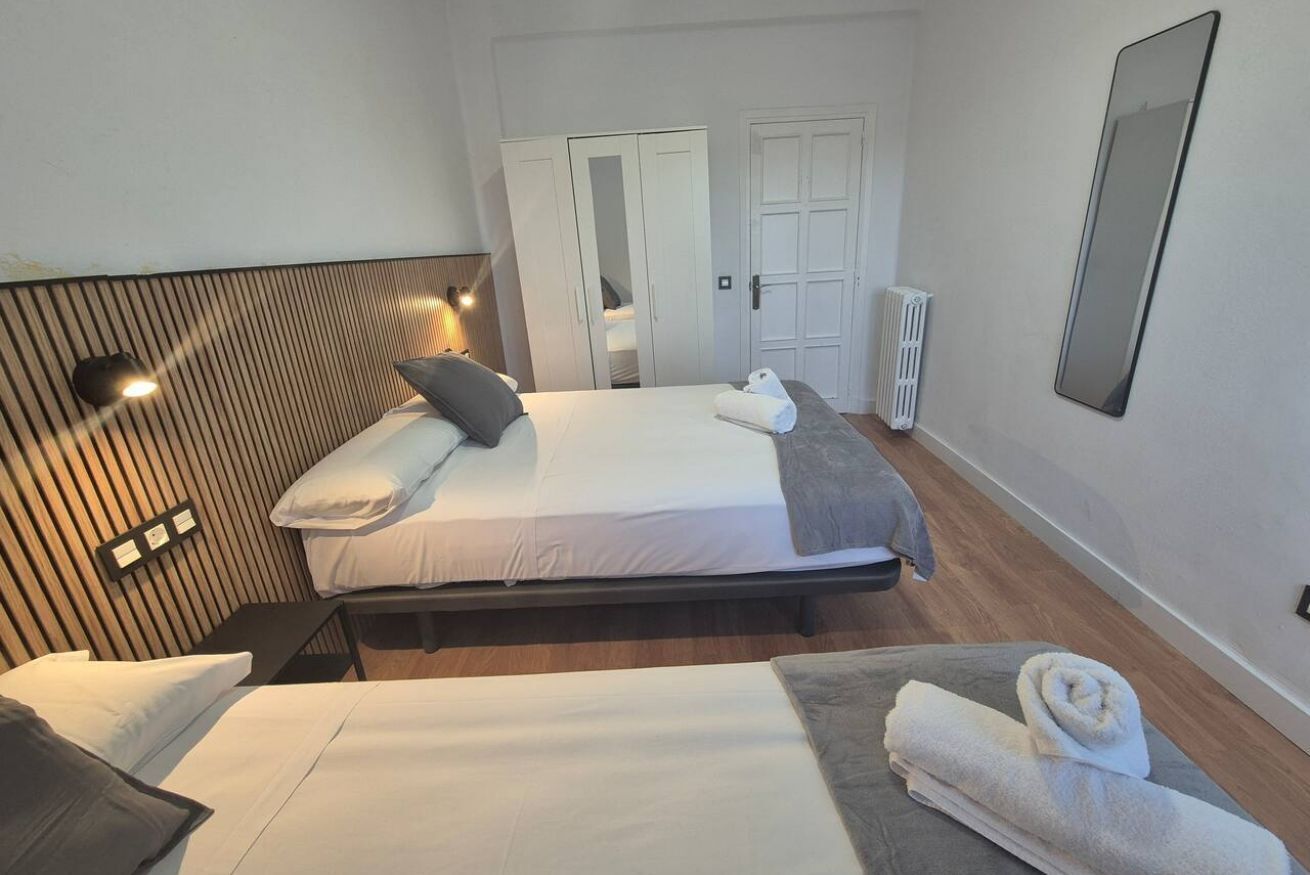 A double bed with a headboard, two bedside tables, a mirror, a radiator, and a wardrobe.