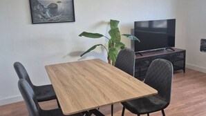 Ein Essbereich mit einem Holztisch, schwarzen Stühlen, einer großen Grünpflanze und einem Fernseher auf einem Schrank.