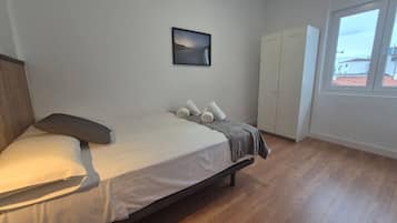 Un dormitorio con cama, armario, ventana y un cuadro en la pared.