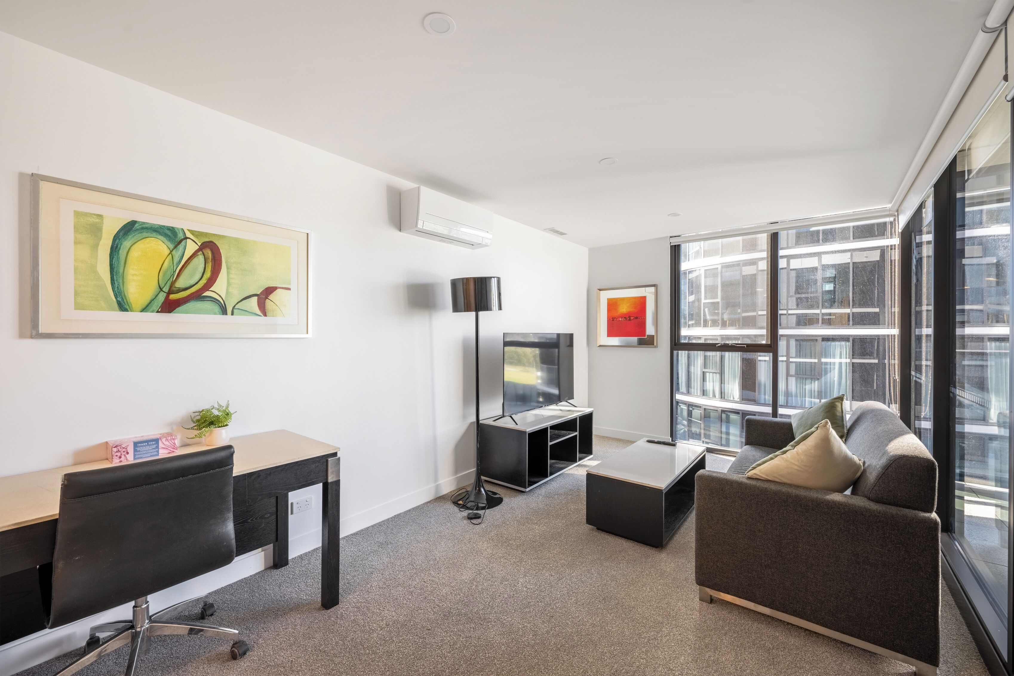 A modern office space with a desk, chair, sofa, and large windows.