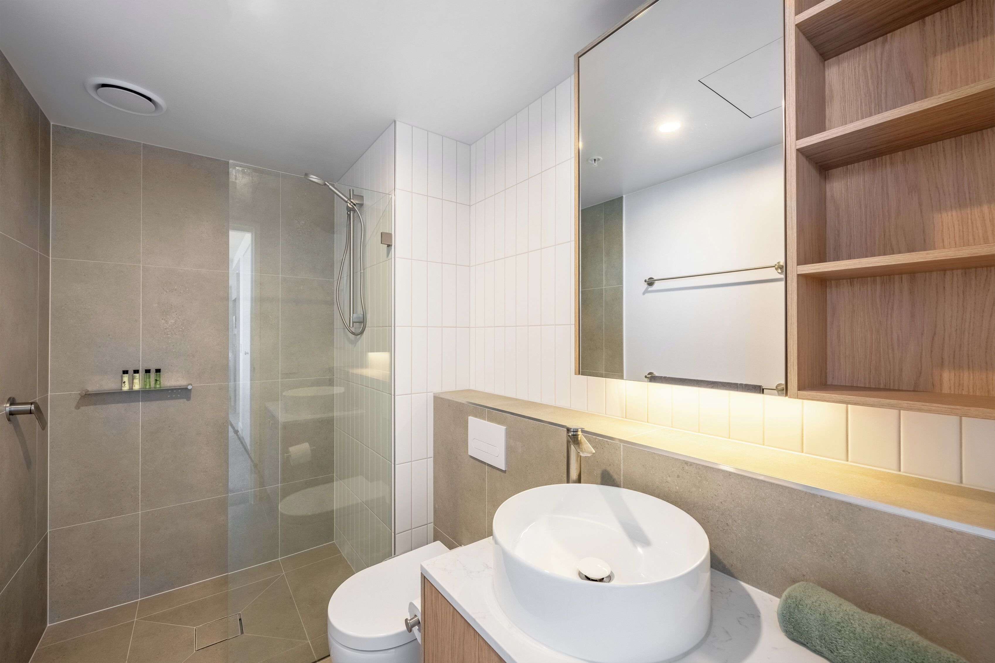 Un baño moderno con ducha envuelta en vidrio, lavamanos blanco y tocador de madera.