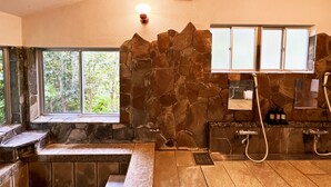 Un baño de piedra con bañera, ducha y ventana.