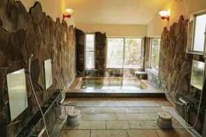 A stone-walled spa with a hot tub, stone benches, and a view of trees. - Vacation Rental Pension Jogasaki (Ito)
