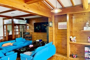 A wooden interior with a blue sofa set, a television mounted on the wall, and a shelf with decorative items. - Vacation Rental Pension Jogasaki (Ito)