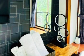 Una habitación con un papel tapiz de diseño geométrico, una ventana con cortinas, un banco de madera y un conjunto de espejos circulares.