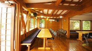 Un interior de madera con una larga mesa, bancos, ventanas amplias y un techo alto.