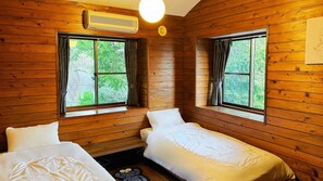 Une cabane avec deux lits, des murs en bois et de grandes fenêtres avec des rideaux.