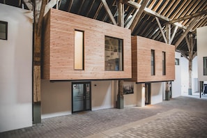 A modern building with wooden paneling, large windows, and a brick-paved ground. - "Fenja" - Cozy maisonette apartment with terrace in the historic courtyard in Rysum - (Rysum)