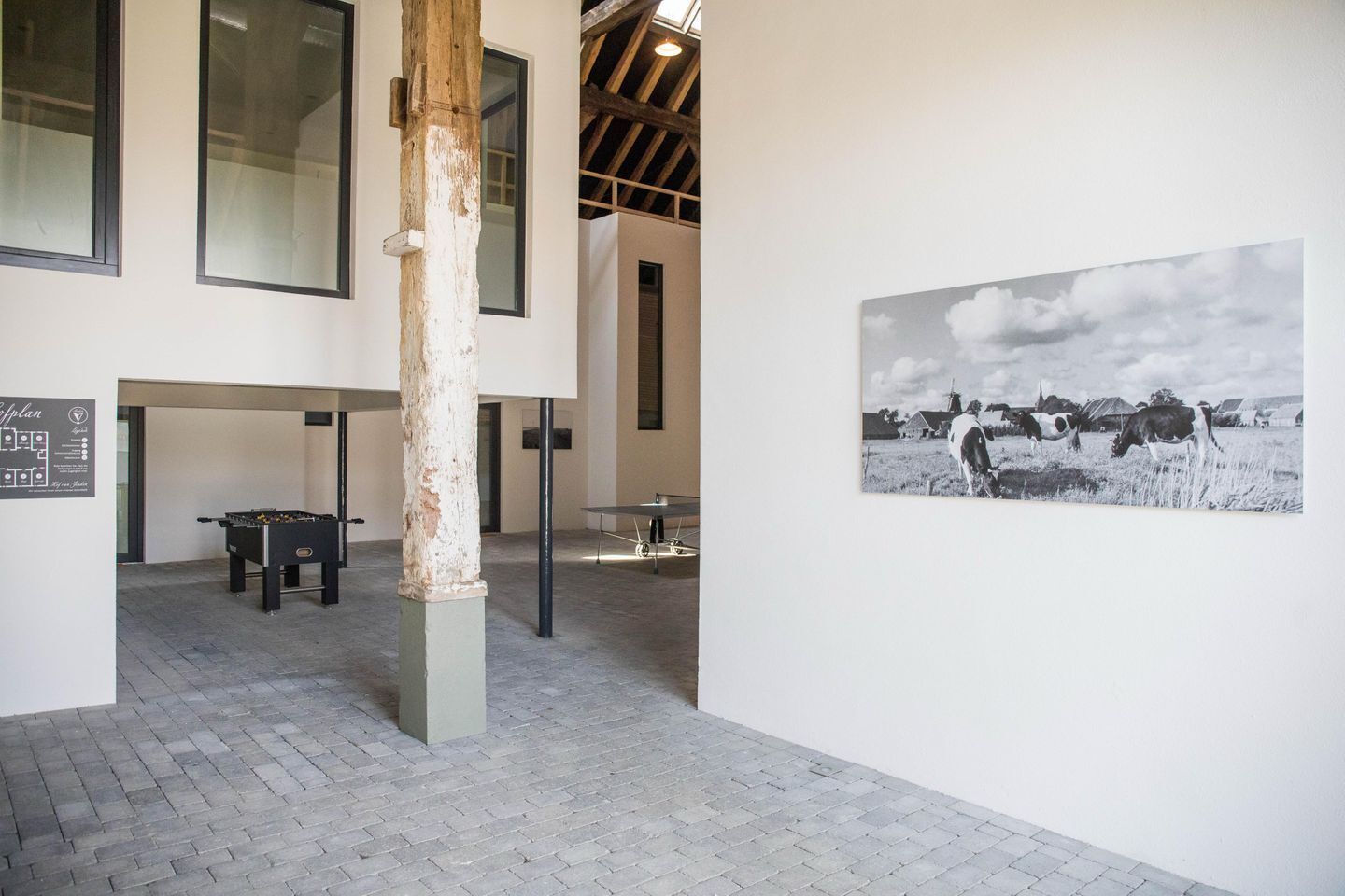 A room with a foosball table, a rustic wooden pillar, and a black and white photograph on the wall.