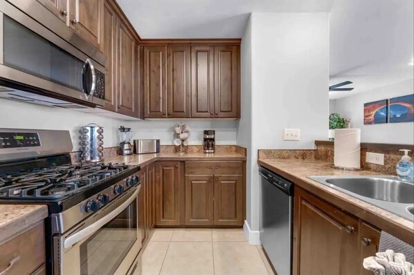 A modern kitchen with wooden cabinets, stainless steel appliances, and a granite countertop. - Red Rock Retreat - Pool/Hot Tub, Park, Yard Games, Basketball and Tennis Courts (Moab)