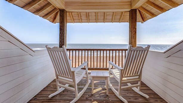 A wooden deck with two rocking chairs facing a beach view.