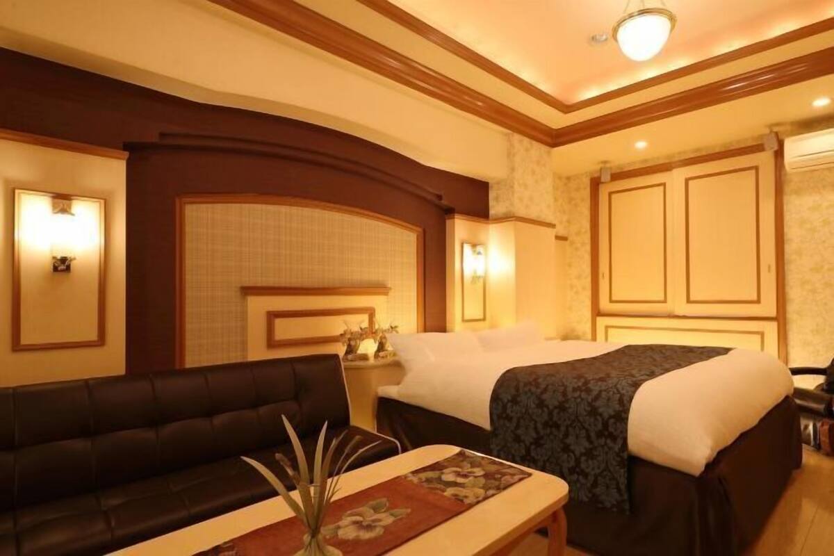Une chambre d’hôtel avec un lit, un canapé, une table de chevet et des lampes fixées au mur.