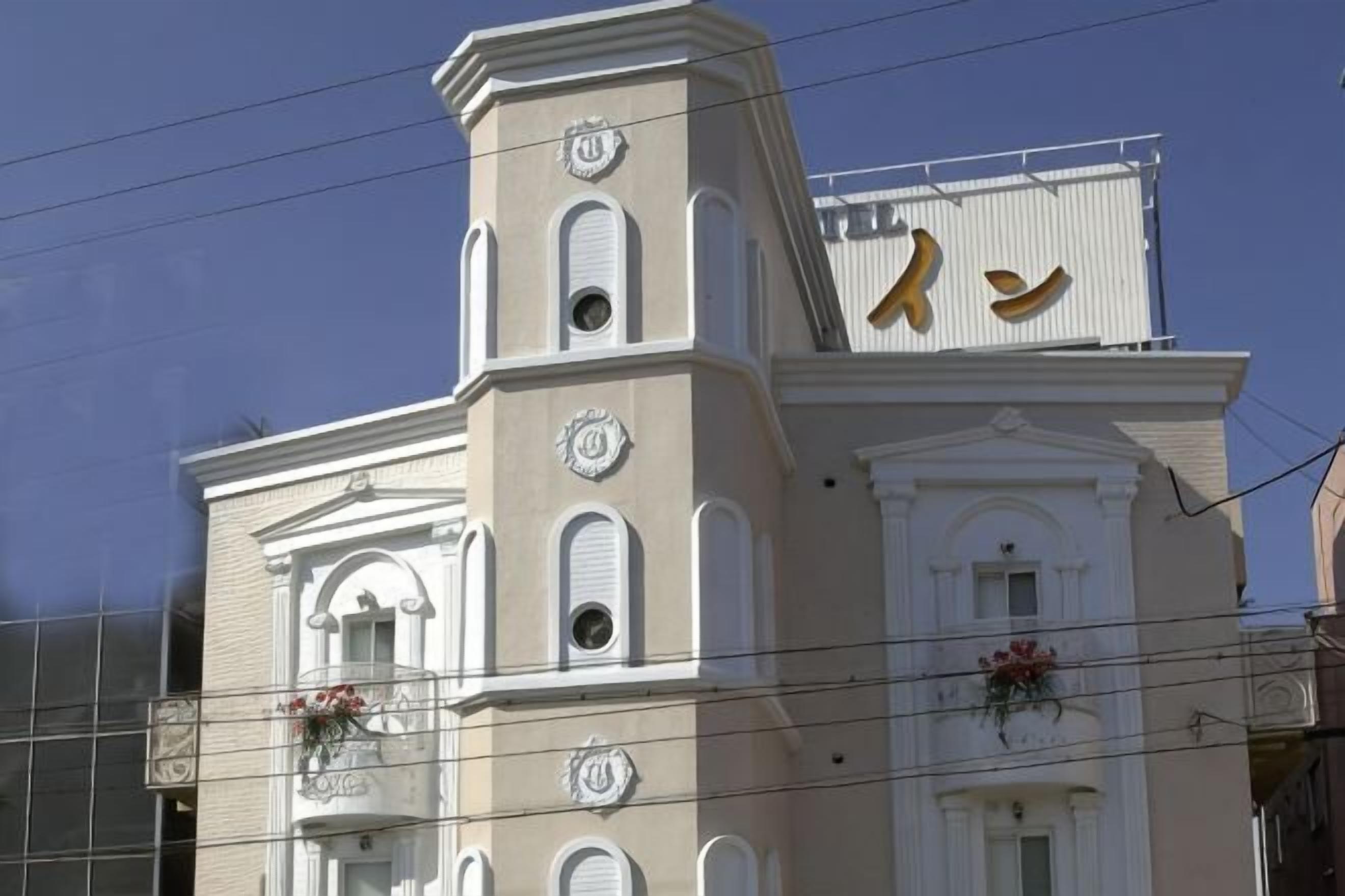 Um edifício com uma torre de relógio, uma varanda florida e uma placa com um símbolo.