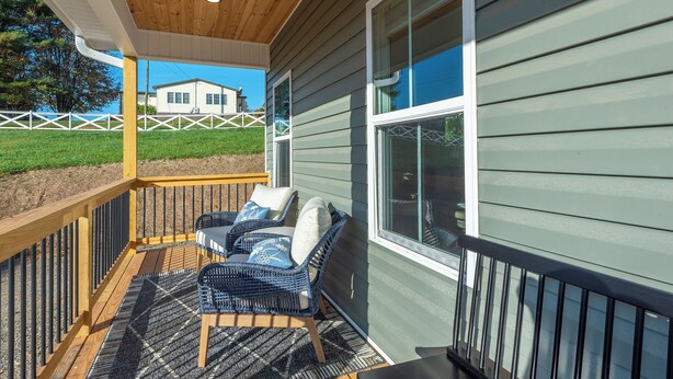 Un espace extérieur aménagé, abrité et doté de meubles en osier et d’une table, ainsi qu’une terrasse en bois, le tout offrant une vue sur une maison en arrière-plan.