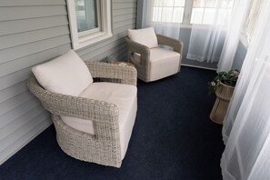 Two wicker sofas with cushions, a dark blue carpet, and a window with sheer curtains.