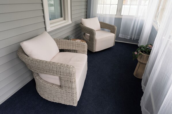 Two wicker sofas with cushions, a dark blue carpet, and a window with sheer curtains.