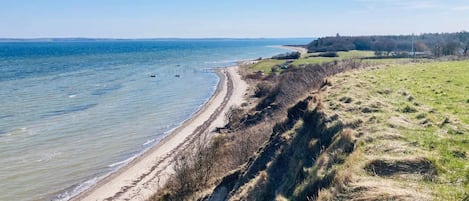 A coastal landscape with a sandy beach, grassy areas, and a clear view of the sea.