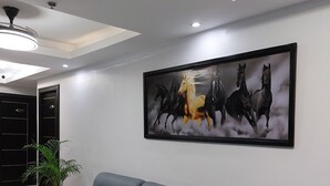 A modern living room with a grey sofa, a large painting of horses, and a ceiling light fixture.