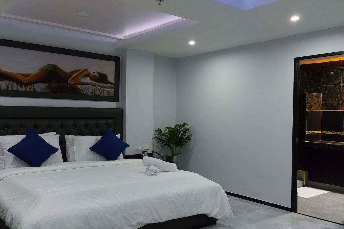 A modern bedroom with a large bed, a ceiling light, and a wall-mounted TV.