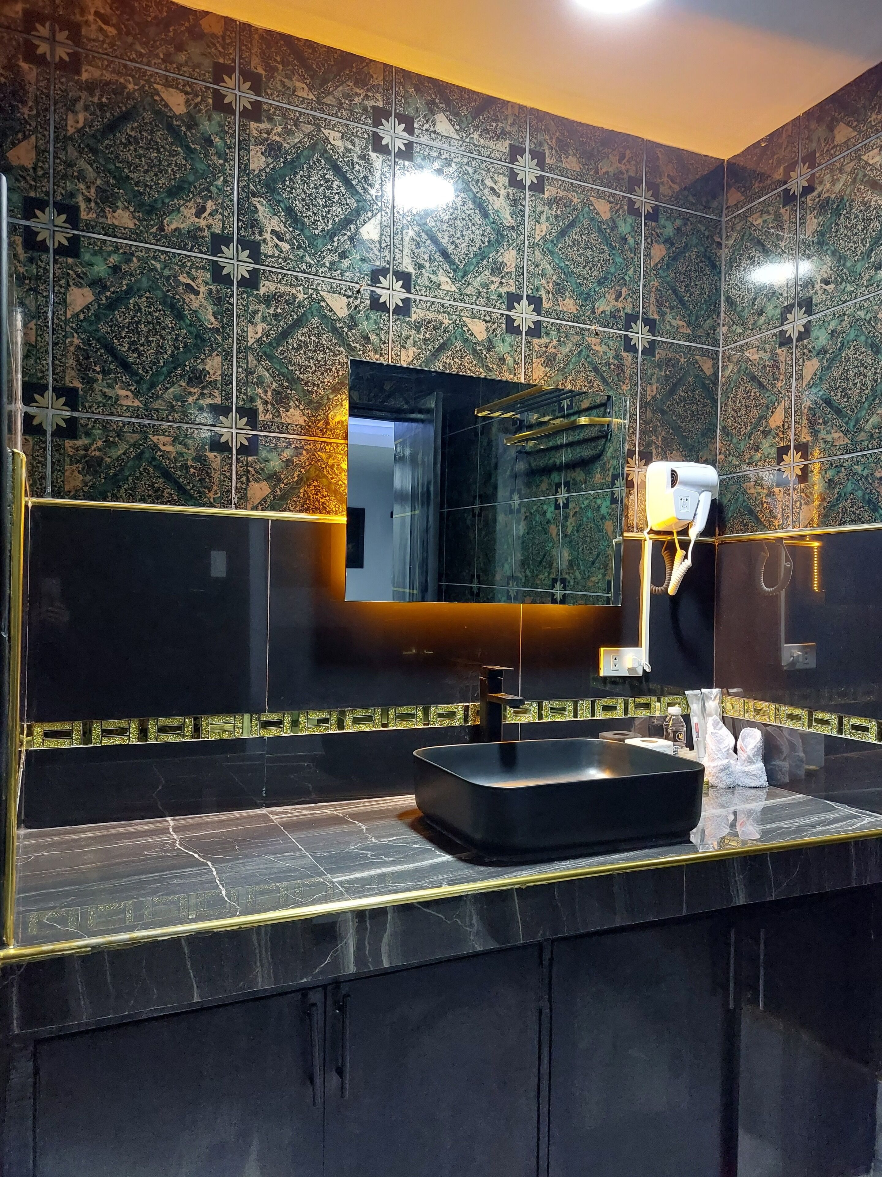 A modern bathroom with a black sink, a large mirror, and a wall with a geometric tile pattern.