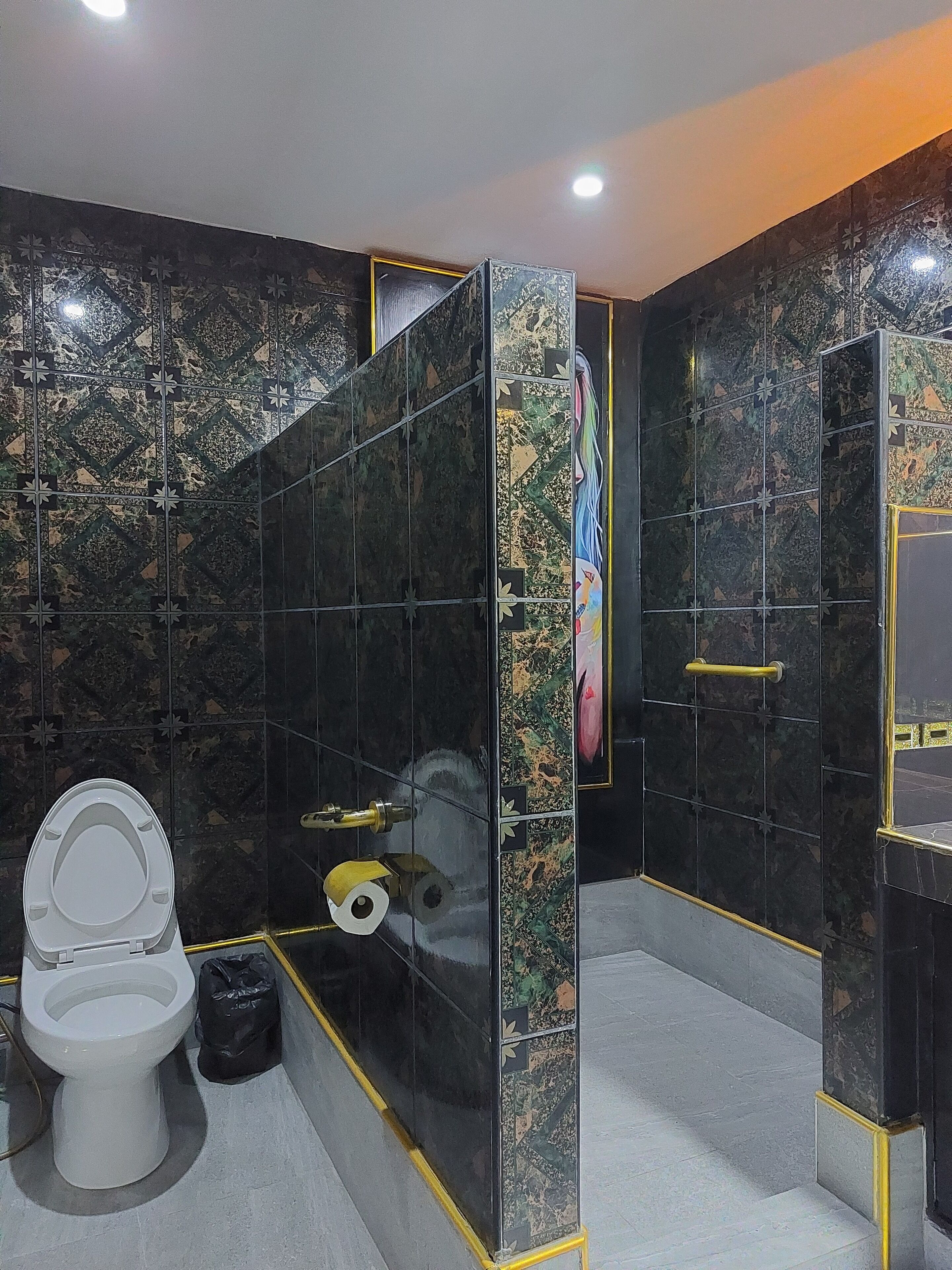 A bathroom with a toilet, a trash bin, and a shower area with a glass partition.