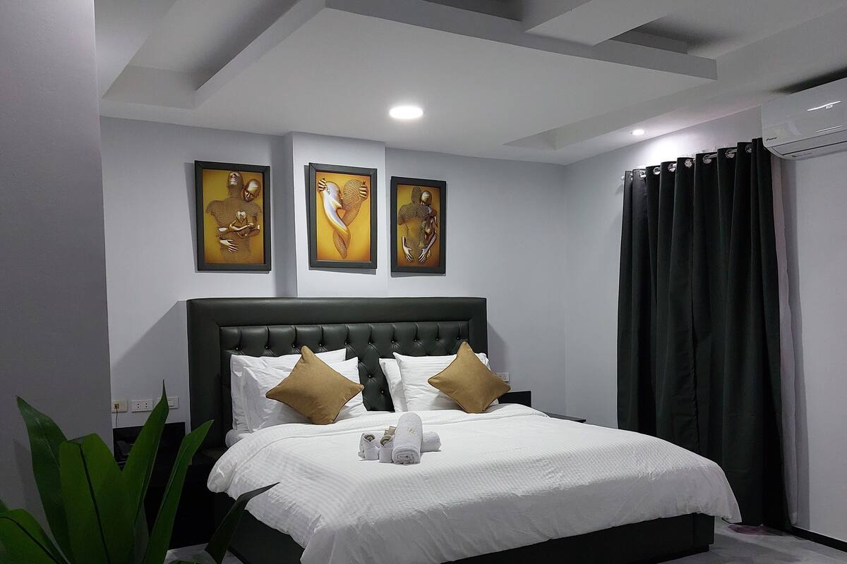 A modern bedroom with a large bed, a headboard, and three framed artworks on the wall.