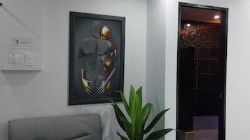 A modern interior with a grey sofa, a framed abstract artwork, a potted plant, and a doorway leading to a darker room.